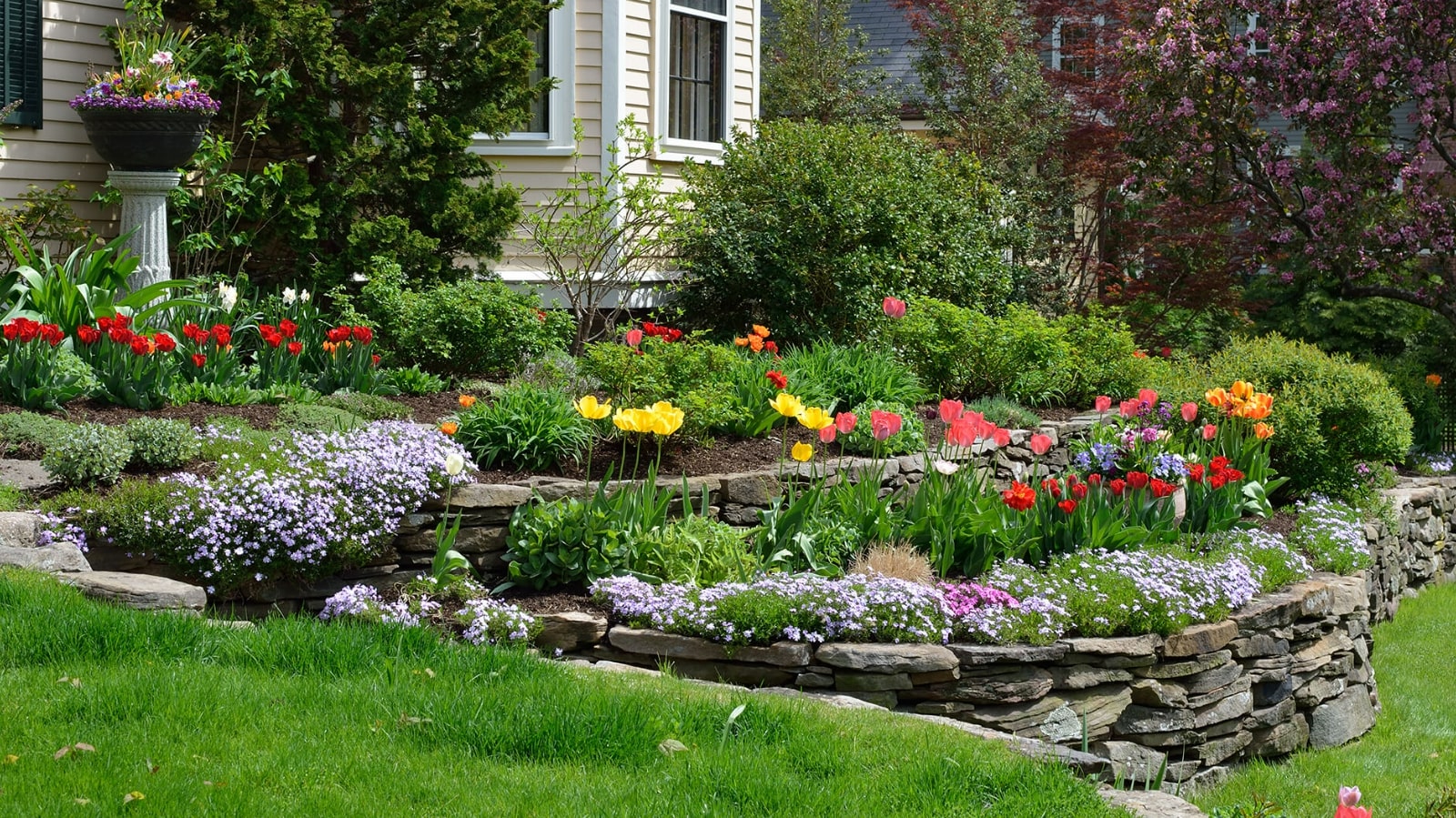 Residential Hardscaping A vibrant flower garden blooms in front of a charming house, showcasing a variety of colorful blossoms and greenery.